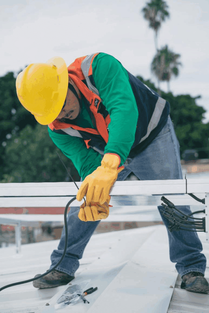 A construction worker fixing wires on a roof.