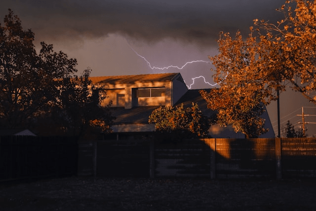 This photo shows a metal-roofed house with lightning flashing behind it