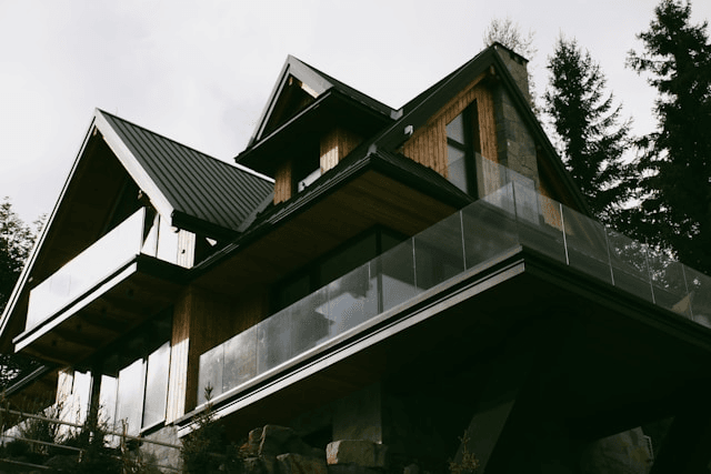 This photo shows a beautiful modern house with a metal roof and a glass balcony