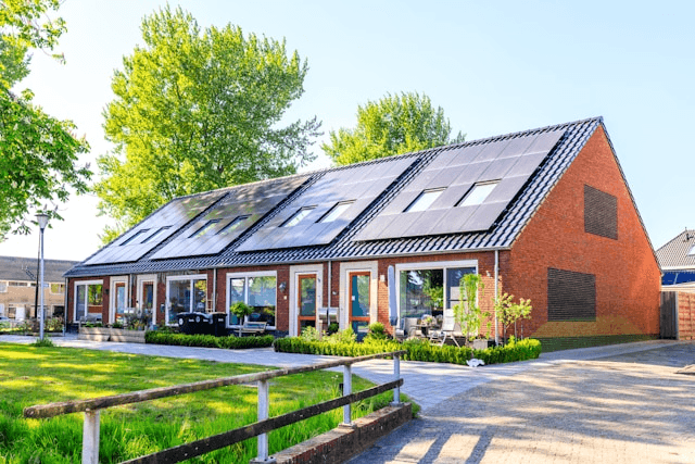 This photo shows a modern house with solar panels, greenery, and sunlight