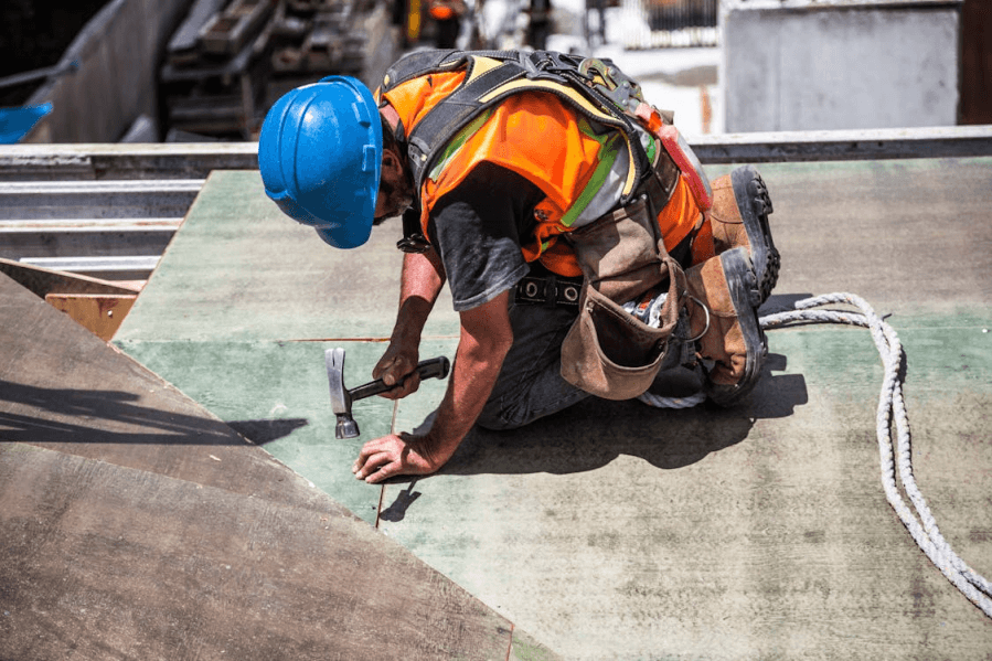 An image of a man wearing a blue helmet and an orange jacket while working on a roof.